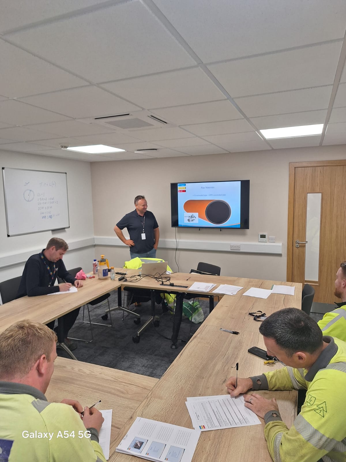 A trainer presenting to course delegates in hi-vis in a training room